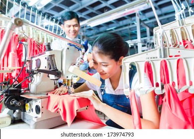 Asian Seamstress or worker in a textile factory sewing with a industrial sewing machine, she is very accurate, the manager looking pleased at her work - Powered by Shutterstock