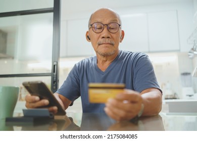 Asian Senior Adult Man Using Credit Card For Online Purchase On Smartphone, Chinese Male Making Online Payment Paying For Service At Home.