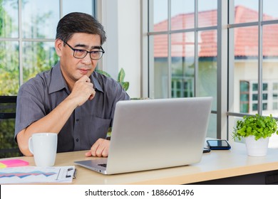 Asian Senior Business Man Working Online On A Modern Laptop Computer He Looking At The Screen For Remote Online Studying. Old Businessman People Using The Laptop To Video Call Conference On Desk Table