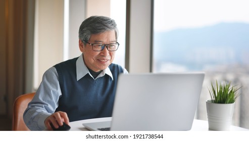 asian senior businessman use laptop to work near window at home