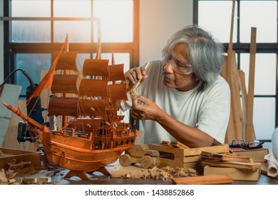 Asian senior carpenter furnishing wooden ship in home workshop - Powered by Shutterstock