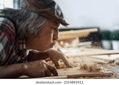 Asian senior carpenters working in the workshop, blowing dust off of a piece of wood, concept of  works in a carpentry shop - Powered by Shutterstock