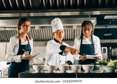 Asian senior chef in uniform teaches cooking techniques to multiracial students. Emphasizing teamwork learning and note-taking in this professional kitchen workshop. Food Edocation - Powered by Shutterstock