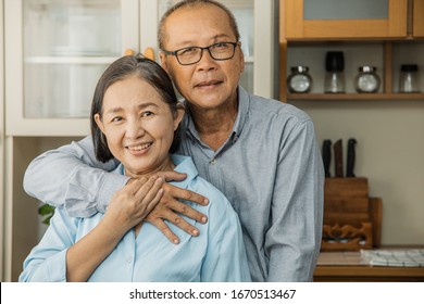 Asian  Senior Couple Is Dancing And Smiling While Cooking Together In Kitchen.