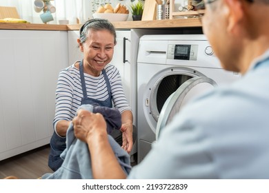 Asian Senior Couple Doing House Working And Chores In Kitchen At Home. Active Elderly Mature Grandparents Clean And Put Clothes In Washing Machine For Laundry, Enjoy Retirement Life In House Together.