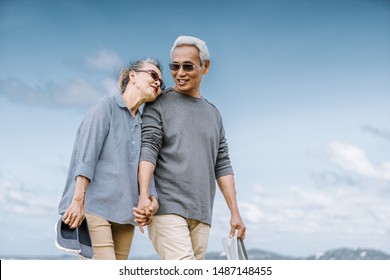 Asian Senior Couple Or Elderly People Walking And Siting At The Beach On Their Weekend Vacation Holiday. Retirement Vaction Concept.