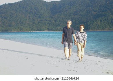 Asian Senior Couple Hand In Hand Happily Walking On The Beach, Concept For Elderly People Lifestyle, Family,travel,vacation,quality Of Life                               