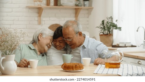 Asian senior couple kindly embracing their teen granddaughter at kitchen table, enjoying their togetherness - family times, relationship, love concept  - Powered by Shutterstock