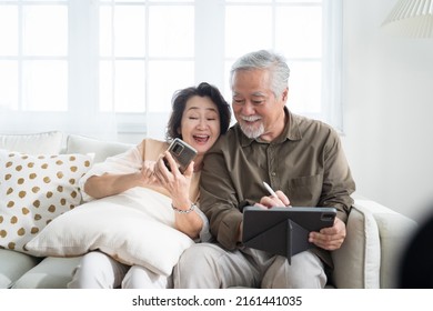 Asian senior couple in living room at home.Wife browsing online on smartphone showing something to her husband while husband is also using a tablet. - Powered by Shutterstock