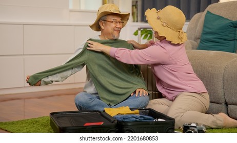 Asian Senior Couple Packing Clothes And Stuff For Travel Trip Together At Home, Senior Retired Couple Enjoying To Arrange Clothes In Living Room, Senior Husband And Wife Organizing Clothes Baggage