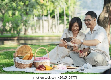 Asian Senior Couple Relaxing with Wine and Smartphone During Picnic in Park - Powered by Shutterstock