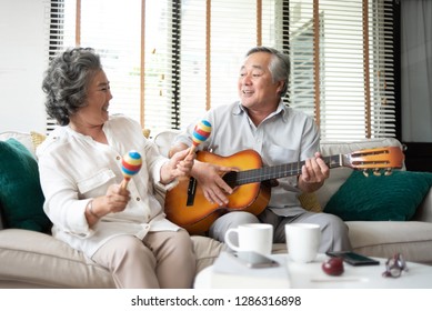 Asian senior Couple singing and playing acoustic guitar together. Elderly man, woman having fun with String instrument. Older people enjoying while sitting in couch at house. life, Lifestyle, Carefree