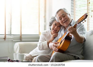 Asian senior Couple singing and playing acoustic guitar together. Smiling Elderly man and woman having fun in the living room at their house. Retirement, Lifestyle, Enjoying, Romantic.