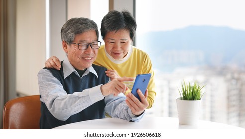 asian senior couple use smartphone near window at home