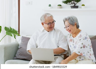 Asian Senior Couple Using Computer Laptop For Internet Searching, Online Shopping, And Buying Insurance At Living Room At Home, Senior With Technology Concept