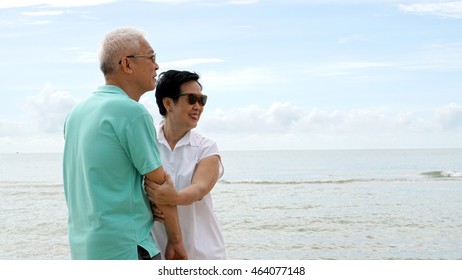 Asian Senior Couple Walking Together On The Beach By The Sea