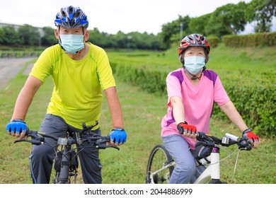 Asian Senior Couple  Wearing Medical Mask And Riding Bicycle In The Park