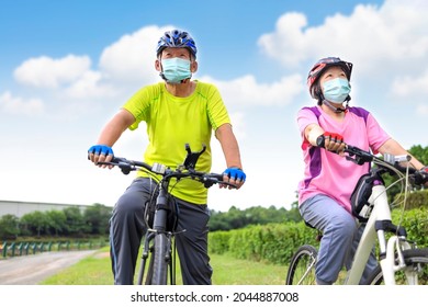 Asian Senior Couple  Wearing Medical Mask And Riding Bicycle In The Park