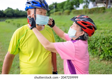 Asian Senior Couple  Wearing Medical Mask And Riding Bicycle In The Park