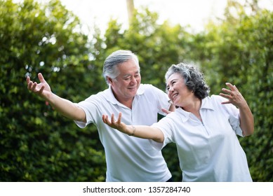 Asian Senior Couple in white shirt practicing Tai Chi in park together. Smiling Elderly people exercise togetherness over green nature at outdoor. Wellness, Lifestyle of old people. Positive emotion - Powered by Shutterstock