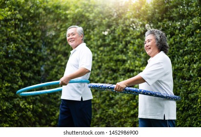 Asian Senior Couple In White Shirt Exercising With Hula Hoops At Outdoor Park Together.