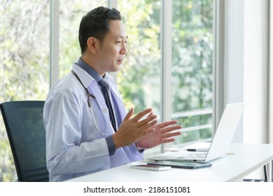 Asian Senior Doctor Sitting In Medical Office While Video Call Meeting Using Laptop Computer.