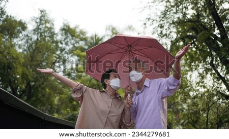 Asian senior elder couple walking in raining park share umbrella romantic love lifestyle
