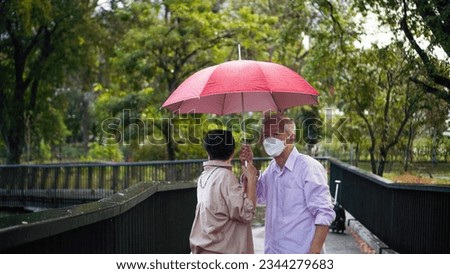 Asian senior elder couple walking in raining park share umbrella romantic love lifestyle