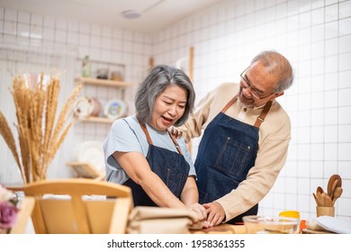 Asian Senior Elderly Couple Standing In Kitchen At House Feeling Happy And Enjoy Retirement Life Together. Loving Older Grandparent Cooking Food With Smiling Face. Relationship And Activity At Home.
