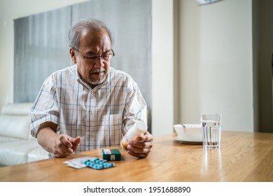 Asian Senior elderly male patient sitting alone in house nursing care. Mature older man looking to medicine pills bottle and read prescription and contents of the medicine in hand after eating food. - Powered by Shutterstock