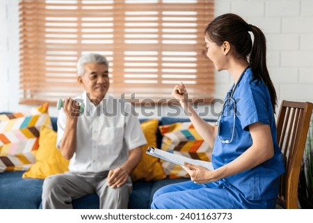 Asian senior elderly man doing physiotherapist with support from nurse. Mature older male patient sit on sofa in living room, using dumbbell exercise with young caregiver at home health nursing care.