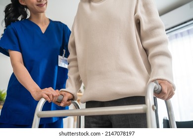 Asian senior elderly man patient doing physical therapy with caregiver. Attractive specialist carer women help and support older mature male practice walking slowly with walker at nursing home care.