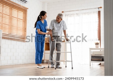 Asian senior elderly man patient doing physical therapy with caregiver. Attractive specialist carer women help and support older mature male practice walking slowly with walker at nursing home care.