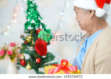Asian senior or elderly old lady woman patient with Santa Claus helper hat holding gift box in christmas and new year celebration festival holiday party in hospital. 
