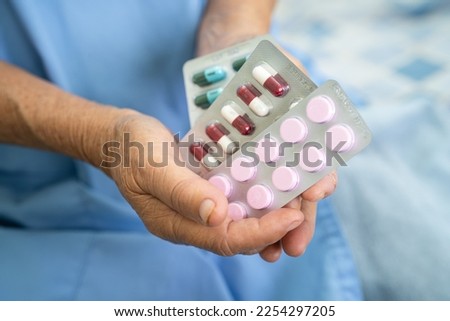 Asian senior or elderly old lady woman patient holding antibiotics capsule pills in blister packaging for treatment infection patient in hospital, Pharmacy drugstore concept.