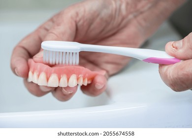 Asian Senior Or Elderly Old Woman Patient Use Toothbrush To Clean Partial Denture Of Replacement Teeth.