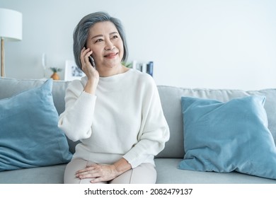 Asian Senior Elderly Woman Smile And Video Call In Living Room At Home. Strong Elderly Older Grandmother Feeling Happy Using Mobile Cell Phone Communicate With Family Enjoy Retirement Life In House.