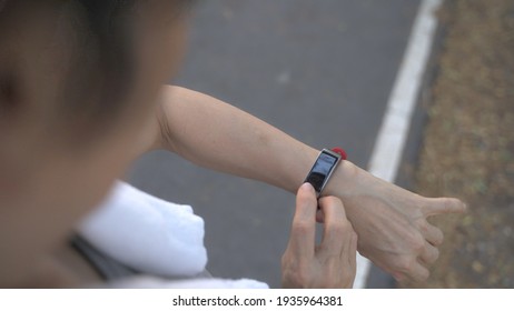 Asian Senior Elderly Woman Touching Smart Watch Activity Tracker At Park Under Tree. Finger Tapping Sport Watch For Calories And Heart Rate Information. Slow Motion Orbit Shot. Health Care Top View.