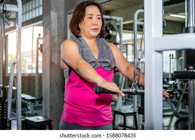 Asian Senior Fat Woman In Sportswear Training Arm With Machine At Gym.