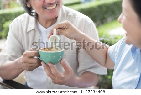 asian senior female pouring syrup to coffee cup, couple asian senior lover talk and drinking coffee in garden, retirement lifestyle
