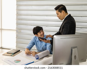 Asian Senior Good-looking Boss In Suit Sitting At Desk And Working With Junior Employee In Office With Roll Of Paper. Businessmen Teamwork And Good Colleagues Concept.