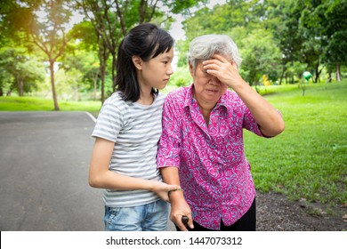 Asian Senior Grandmother Has Headache,touch Her Head With Her Hands,vertigo;dizziness;sick Elderly Woman Having Heat Stroke,sunburn,feel Faint,child Girl Or Granddaughter Care,help,support In Outdoor