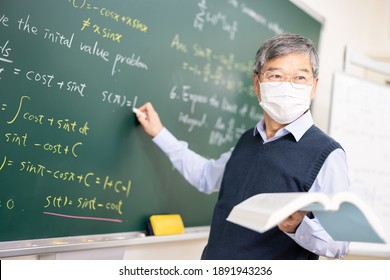 Asian Senior Male Calculus Professor Wearing Face Mask  Is Writing On Blackboard In The Classroom At College