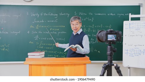 Asian Senior Male Calculus Professor Is Ponting On Board While Having Blackboard Camera Online Through Smartphone In The Classroom At College