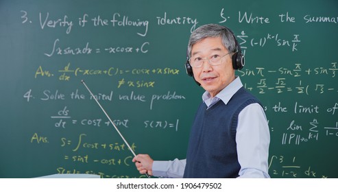 Asian Senior Male Calculus Professor Wearing Headset Is Ponting On Board While Having Blackboard Lecture Online At College