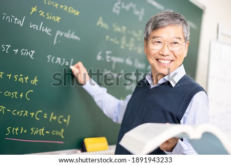 asian senior male calculus professor is writing on blackboard in the classroom at college