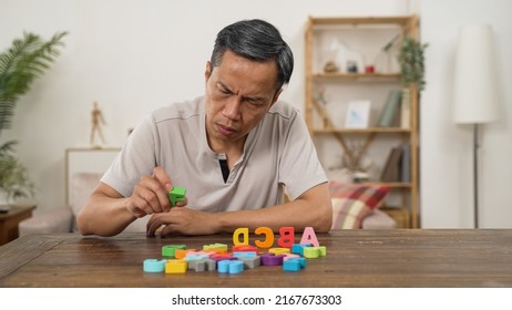 Asian Senior Male With Dementia Trying To Recognize And Arrange Color Letter Blocks In Order At Home. In-home Care And Brain Exercise For Rehabilitation Concept