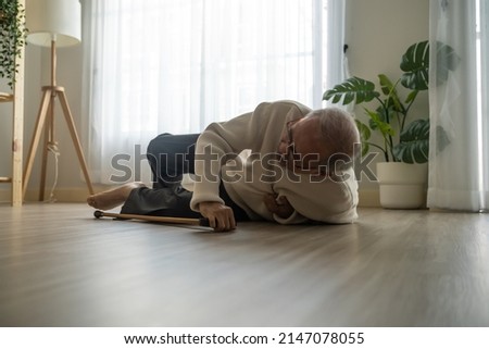 Asian senior male falling on the ground while walk with walker at home. Elderly older mature grandfather having an accident after doing physical therapy alone after retirement in living room in house.