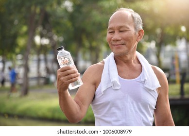 Asian Senior Male Holding Bottle Of Water For Drinking While Exercise At Park Outdoor Background.