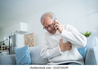 Asian Senior Man Calling Hospital While Feel Having Chest Pain Heart. Attractive Older Mature Patient Using Phone Call To Doctor Has Difficulty Breath Clutch His Chest From Acute Pain In Living Room.